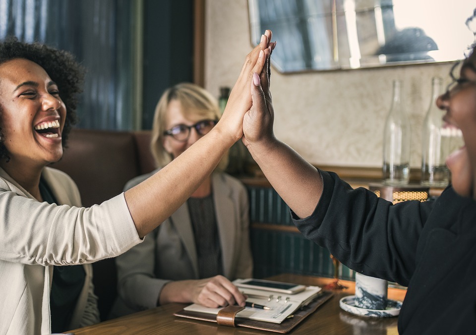 Three diverse women sitting at a table, giving the high five