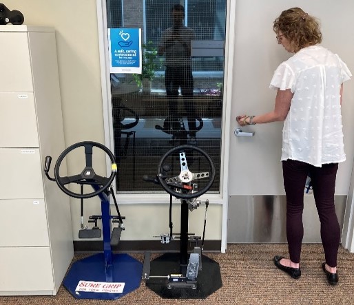 Woman stands next to two steering wheels used to test driving capabilities.