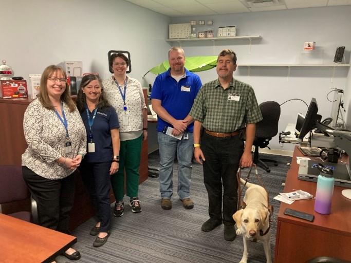 Five people standing together with a service dog on the right.