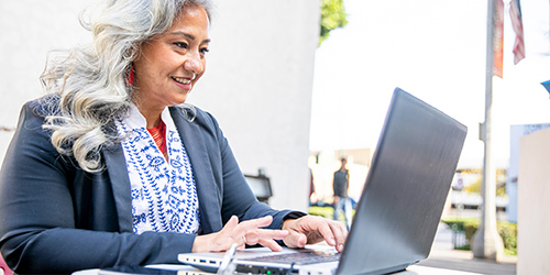 Older woman sitting at a table working on a laptop.