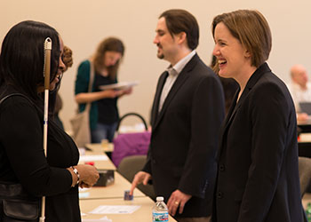 people standing behind tables, one greeting a person with a cane