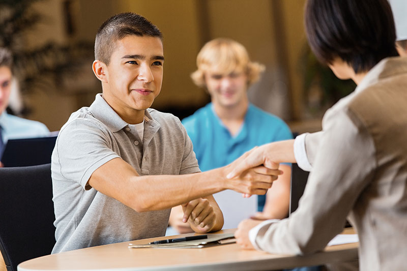 Two teen boys sitting across from each other, shaking hands.